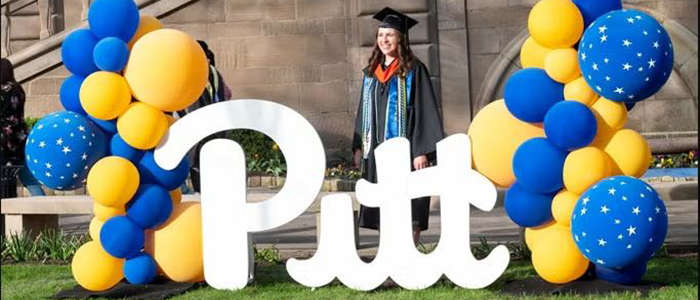 Graduate in center of frame with blue and yellow balloons on either side of them